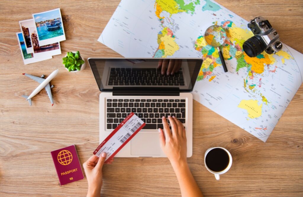 "A person researching how to book a flight online, holding a boarding pass with a laptop, world map, passport, and camera on the desk, symbolizing the process of planning and booking air travel.