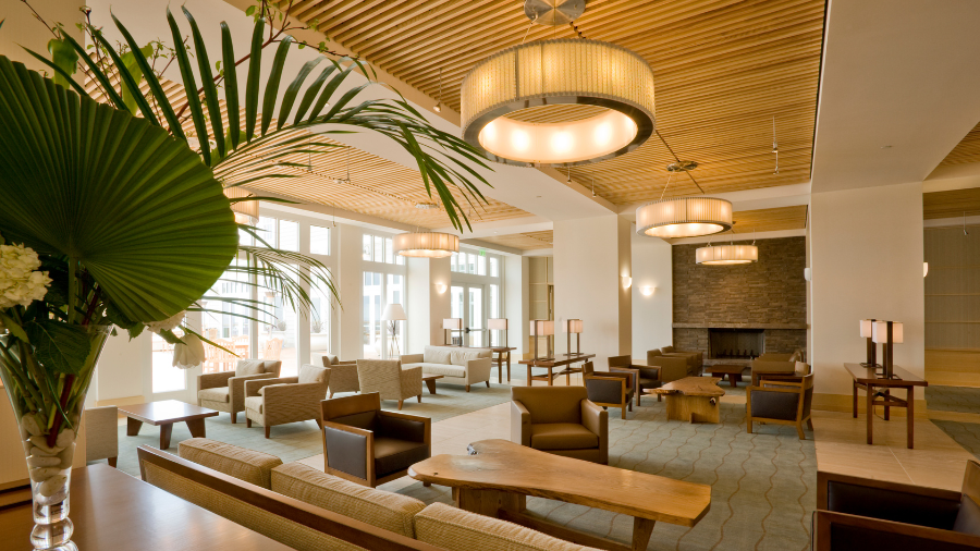 A spacious hotel lobby with contemporary wooden decor, comfortable seating, large windows, and warm ambient lighting.