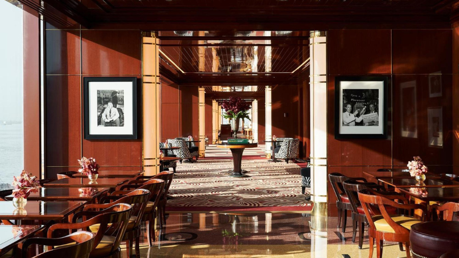 A luxurious dining and lounge area with rich wooden interiors, framed black-and-white photographs, and large windows offering a view of the water.