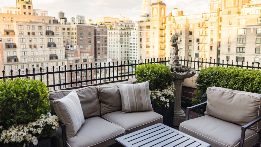 A cozy rooftop terrace with cushioned seating, greenery, and a decorative fountain, overlooking a cityscape of historic buildings.