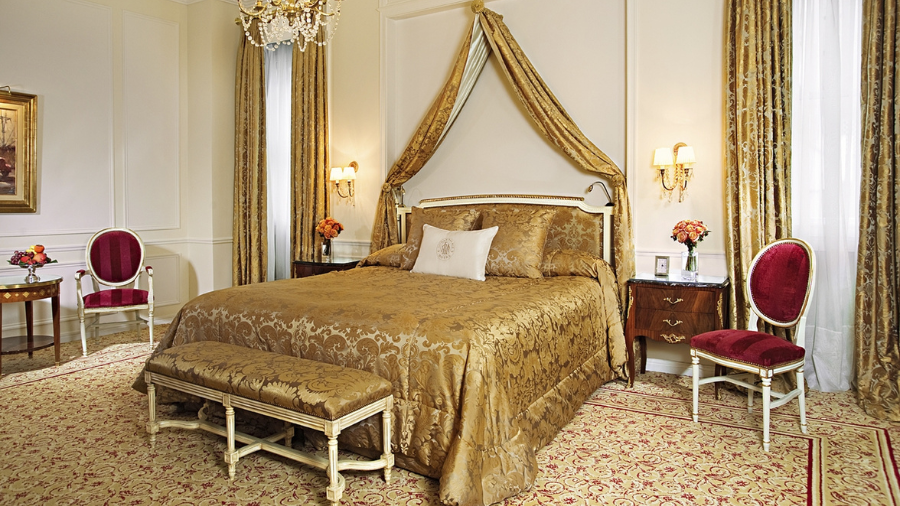 A luxurious hotel suite with gold decor, a grand canopy bed, and elegant furnishings in a classic European style.